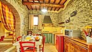 Une cuisine rustique aux murs de pierre, avec une table à manger dressée pour deux personnes, un réfrigérateur rouge et un four à micro-ondes posé sur le plan de travail.