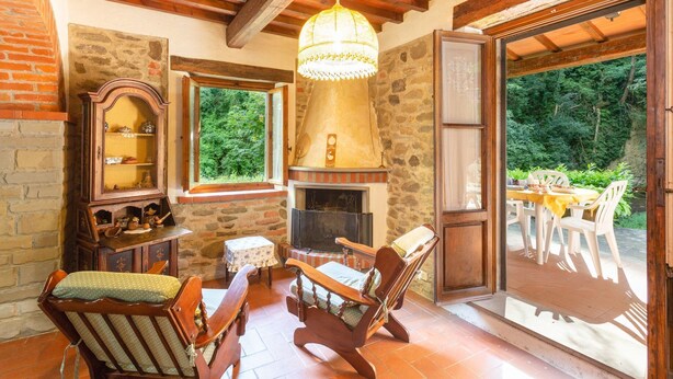 Ein rustikales Interieur mit Kamin aus Stein, Holzmöbeln und Blick ins Freie.