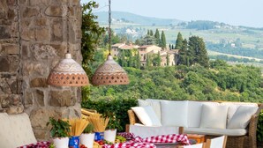A table set for dining with a view of a rural landscape, stone wall, and hanging lamps.