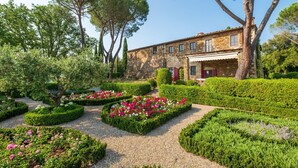 A stone building with a garden featuring neatly trimmed hedges and flower beds.