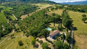 Vue aérienne d’une propriété rurale dotée d’une piscine, entourée d’une végétation luxuriante et de collines.