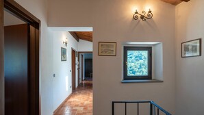Un couloir doté d’un sol carrelé, d’une porte en bois, d’un escalier avec une rampe en métal et d’une fenêtre donnant sur des arbres.