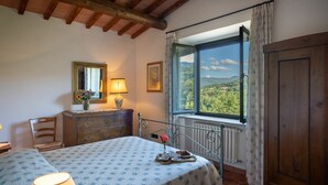 Une chambre à coucher comprenant un lit, une commode, une chaise, une fenêtre donnant sur un espace verdoyant et un radiateur.