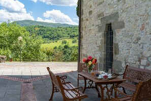 Un patio al aire libre con una mesa de piedra dispuesta para el desayuno, bancos y vistas a un valle verde.