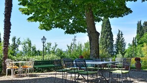 An outdoor seating area with a table and chairs, surrounded by trees and a lamp post. - Villa Buonaparte - Vacation rental near Pisa, Tuscany (Corazzano)