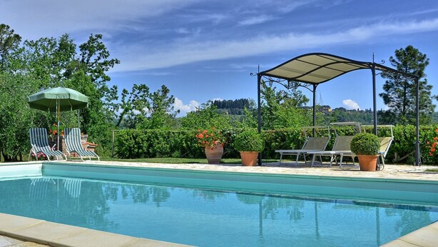A swimming pool with lounge chairs and umbrellas, surrounded by greenery and a clear sky. - Villa Buonaparte - Vacation rental near Pisa, Tuscany (Corazzano)