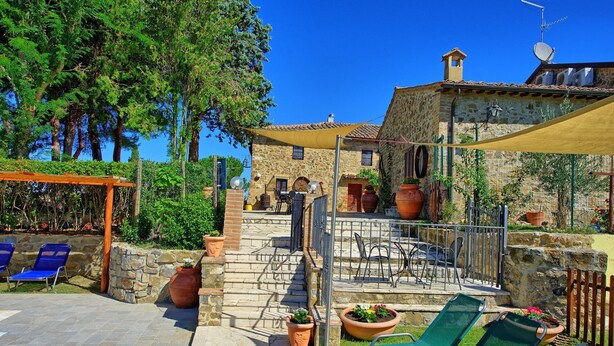 Edificio de piedra con un patio que cuenta con mobiliario exterior, una pérgola y macetas con plantas.