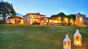 A well-lit courtyard with a grassy lawn, two lit lanterns, and a stone building with multiple windows and a tiled roof. - Villa Sant' Angelo - Villa with private pool (Poppi)