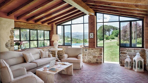 A spacious living area with a stone fireplace, large windows offering a view of the outdoors, and a wooden ceiling. - Villa Sant' Angelo - Villa with private pool (Poppi)