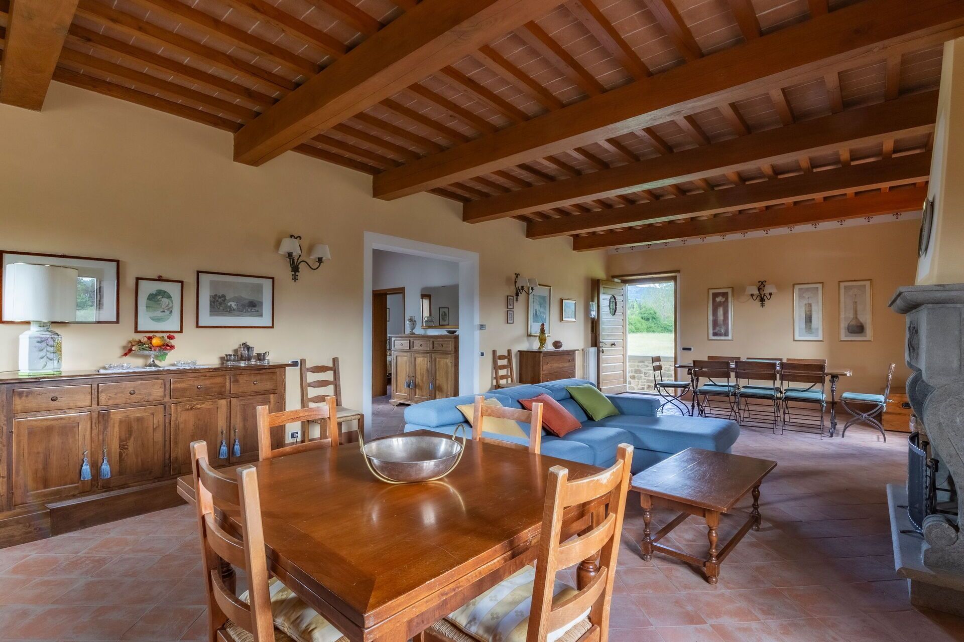 A spacious living area with a wooden dining table, blue sofa, and a stone fireplace.