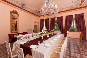 A formal dining room with a long table set for a meal, elegant chairs, and a chandelier.