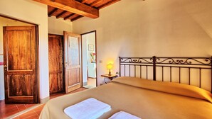 A bedroom with a bed, wooden doors, a nightstand with a lamp, and a tiled floor. - Le Fonti 5 - Apartment with swimming pool (Grassina)