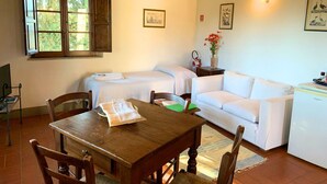 A cozy room with a wooden dining table, two single beds, a white sofa, and a small kitchenette. - Le Fonti 6 - Apartment with swimming pool (Grassina)