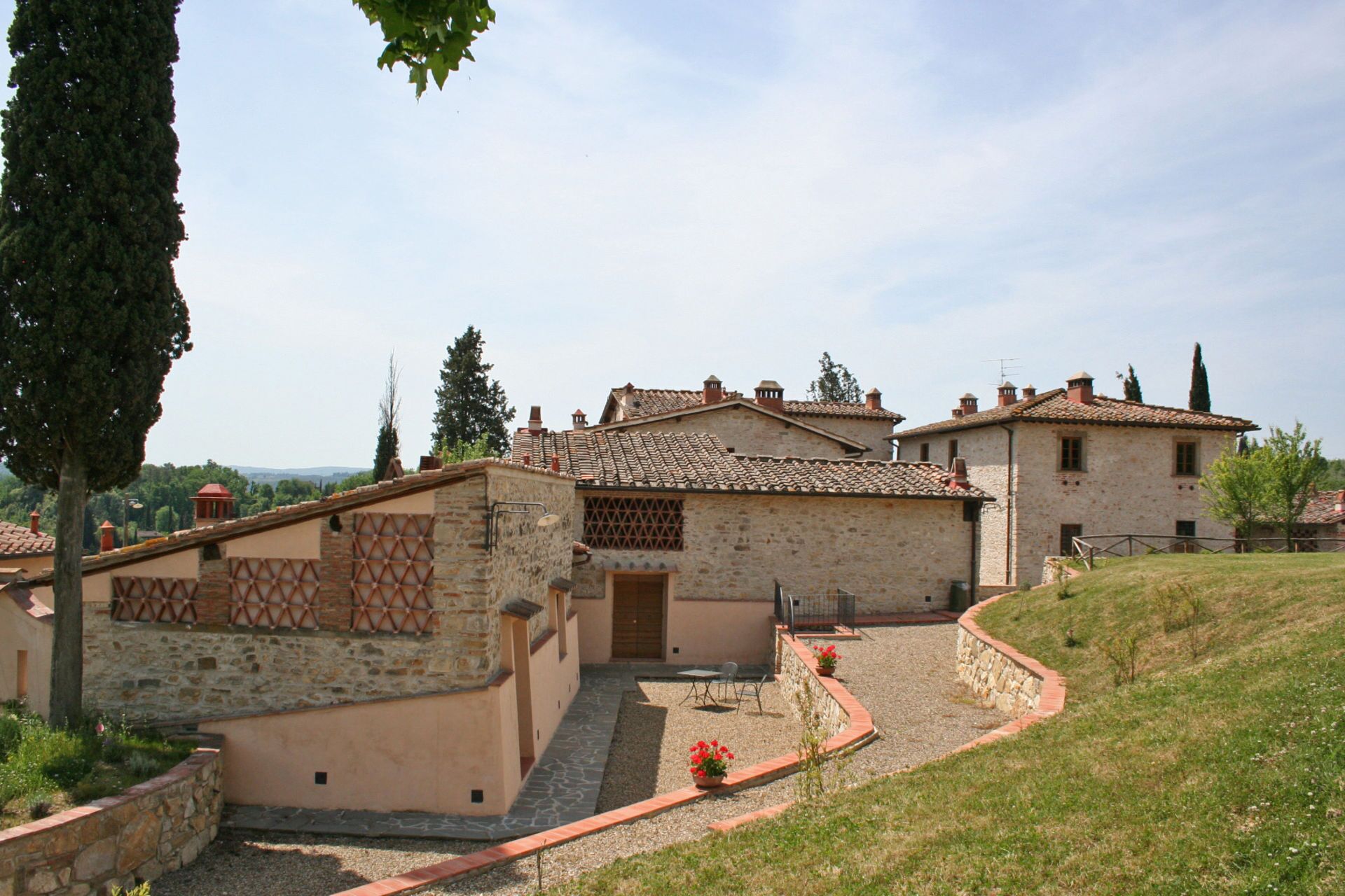 A stone building with a tiled roof, a small garden area with a pathway, and a view of the surrounding landscape.