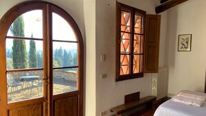 Un dormitorio con un amplio ventanal de arco, una cama, un banco y vistas al exterior.