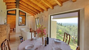 Un comedor con una mesa dispuesta para cuatro, vigas de madera en el techo y vistas al campo a través de amplias ventanas.