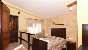 Una camera da letto con un letto, una scrivania in legno, un comodino, una finestra con tende, una ventola a soffitto e una lampada a parete.