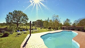 Una piscina con bordo piastrellato, circondata da alberi e un cielo sereno.