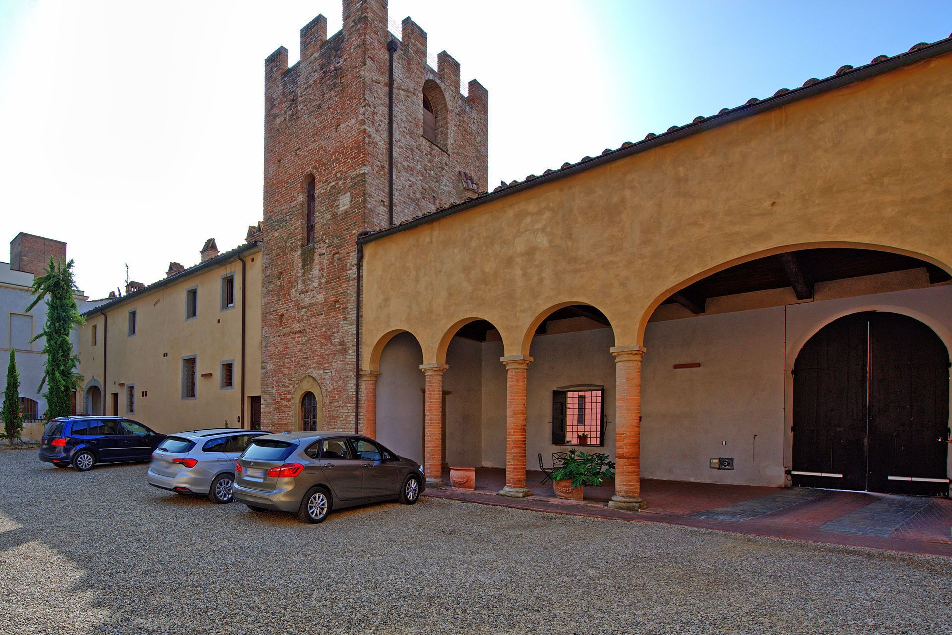 A building with a brick tower and arched entrances. There are cars parked in front.