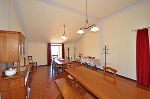 Een ruime eetzaal met een lange houten tafel, meerdere stoelen en een kroonluchter.