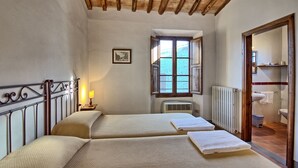 A room with two beds, a window, a radiator, and a bathroom visible through an open door.