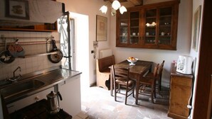 A kitchen with a stove, sink, and wooden cabinets. There is a dining table with chairs and a chandelier above. - Cappella - Apartment with swimming pool (San Polo In Chianti)