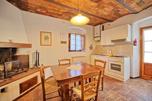 A rustic kitchen with a wooden table and chairs, a stove, and a hanging light fixture.