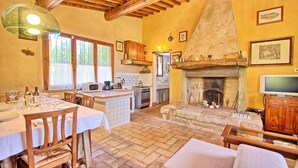 A rustic kitchen with a stone fireplace, wooden beams, and a dining area with a table set for a meal.