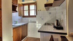 A compact kitchen with wooden cabinets, a window, white tiled backsplash, and a stove.