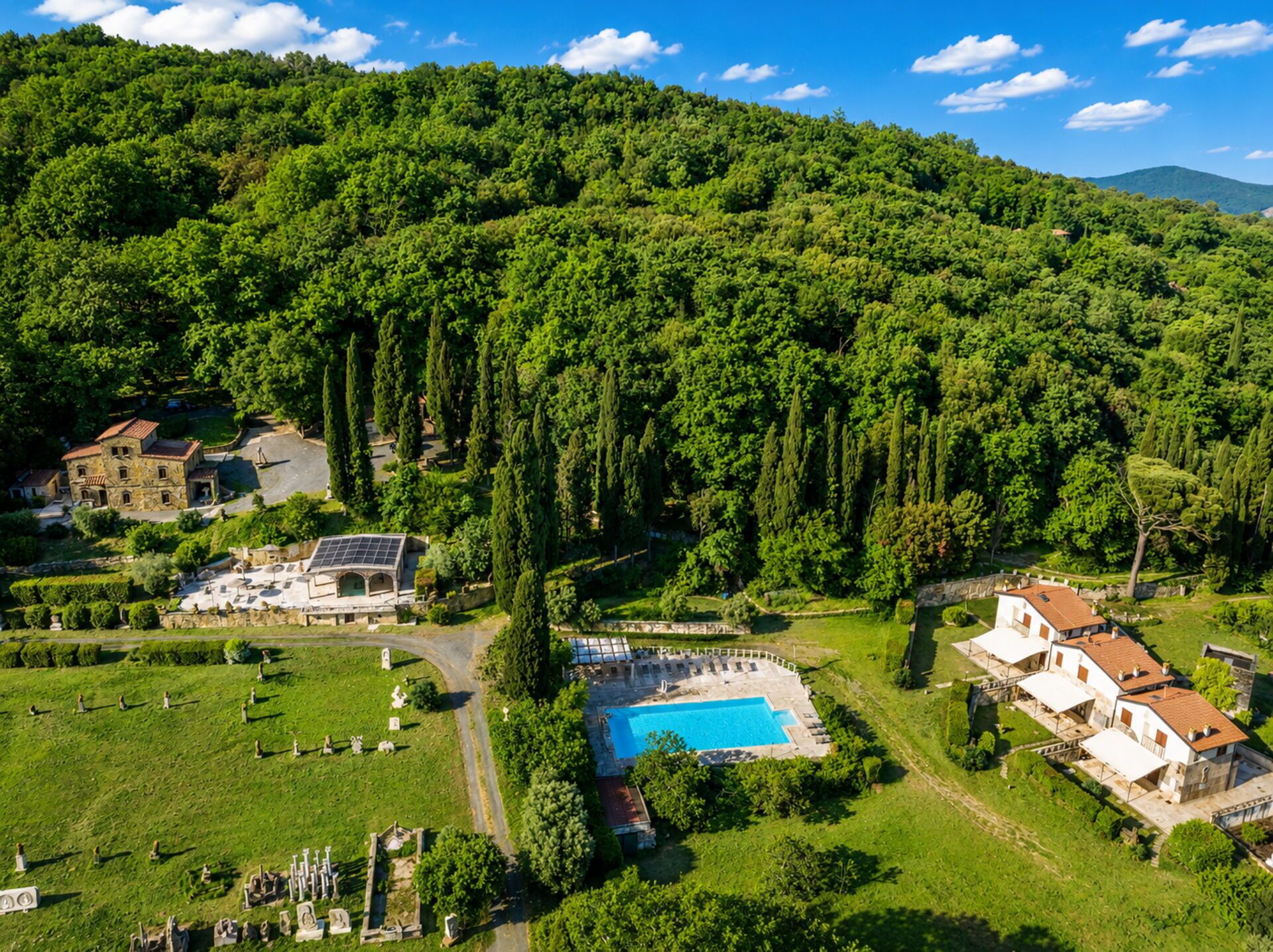 A large villa with a swimming pool, surrounded by lush greenery and a hilly landscape.