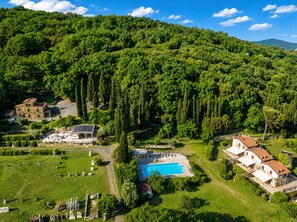 A large villa with a swimming pool, surrounded by lush greenery and a hilly landscape.