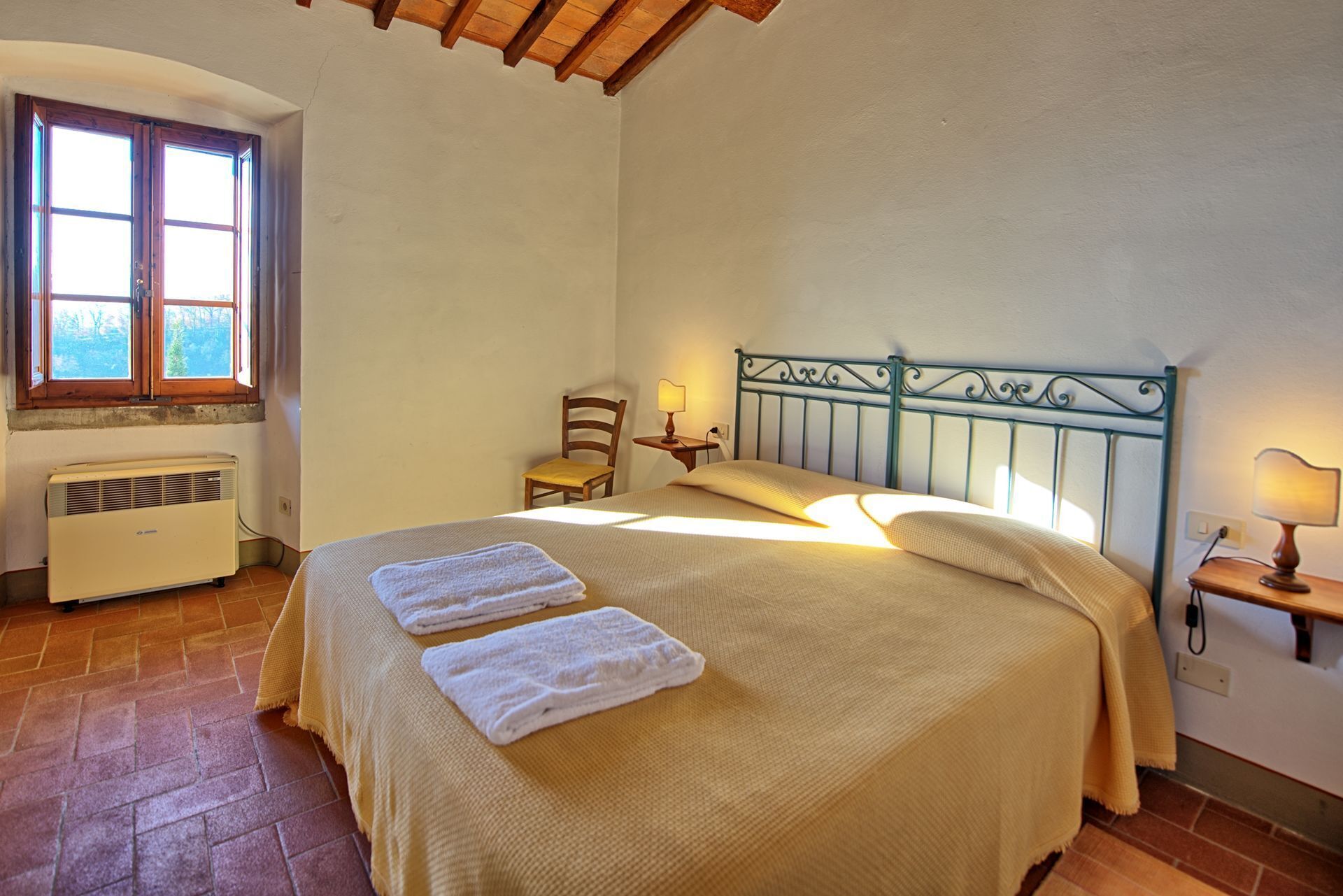 A bedroom with a bed, two bedside lamps, a chair, a window, and an air conditioner.
