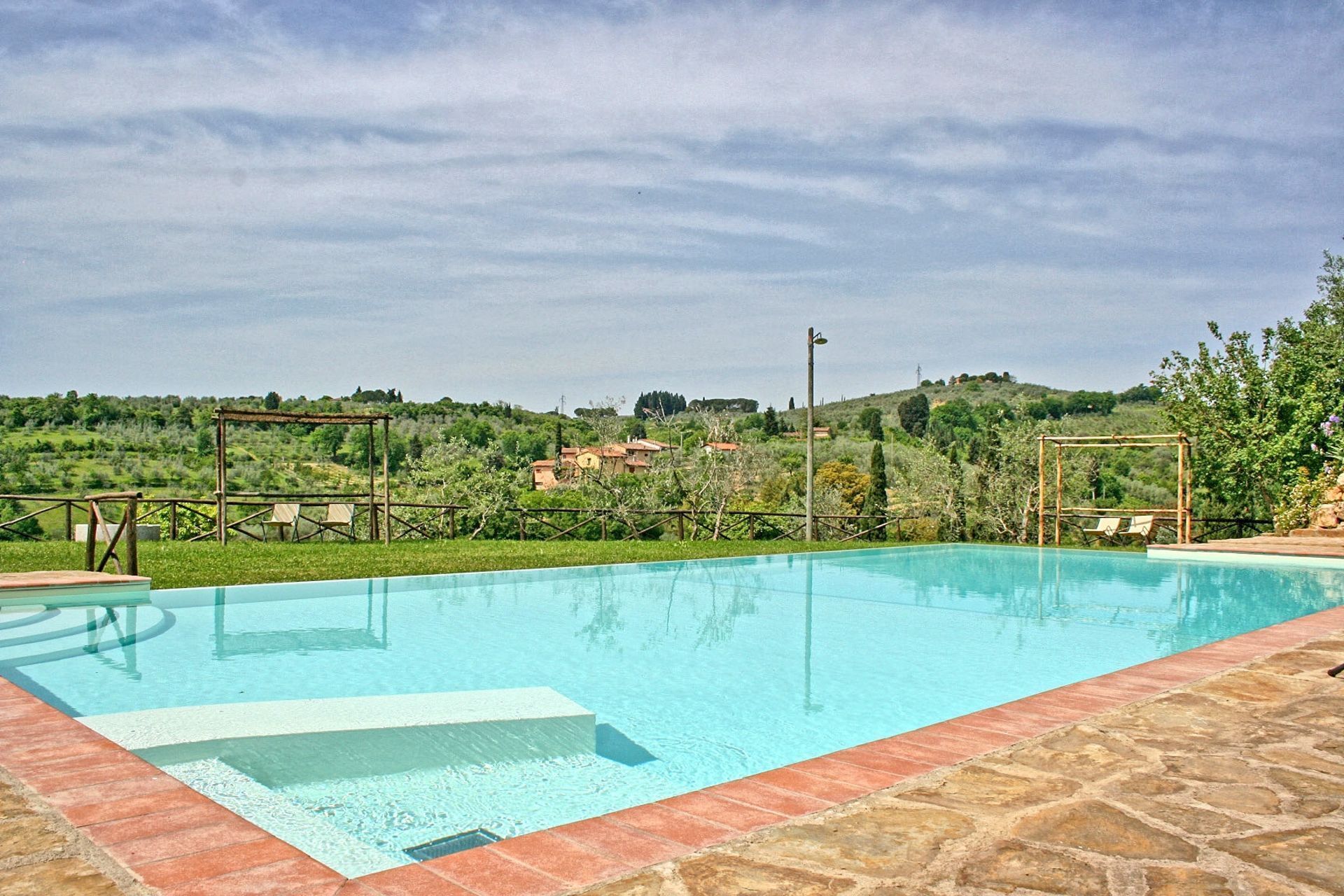 Ein rechteckiger Pool mit Steinrand, umgeben von einer Rasenfläche und einer Holzpergola.