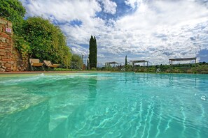 Una piscina cristalina con sillas de descanso y una pérgola.