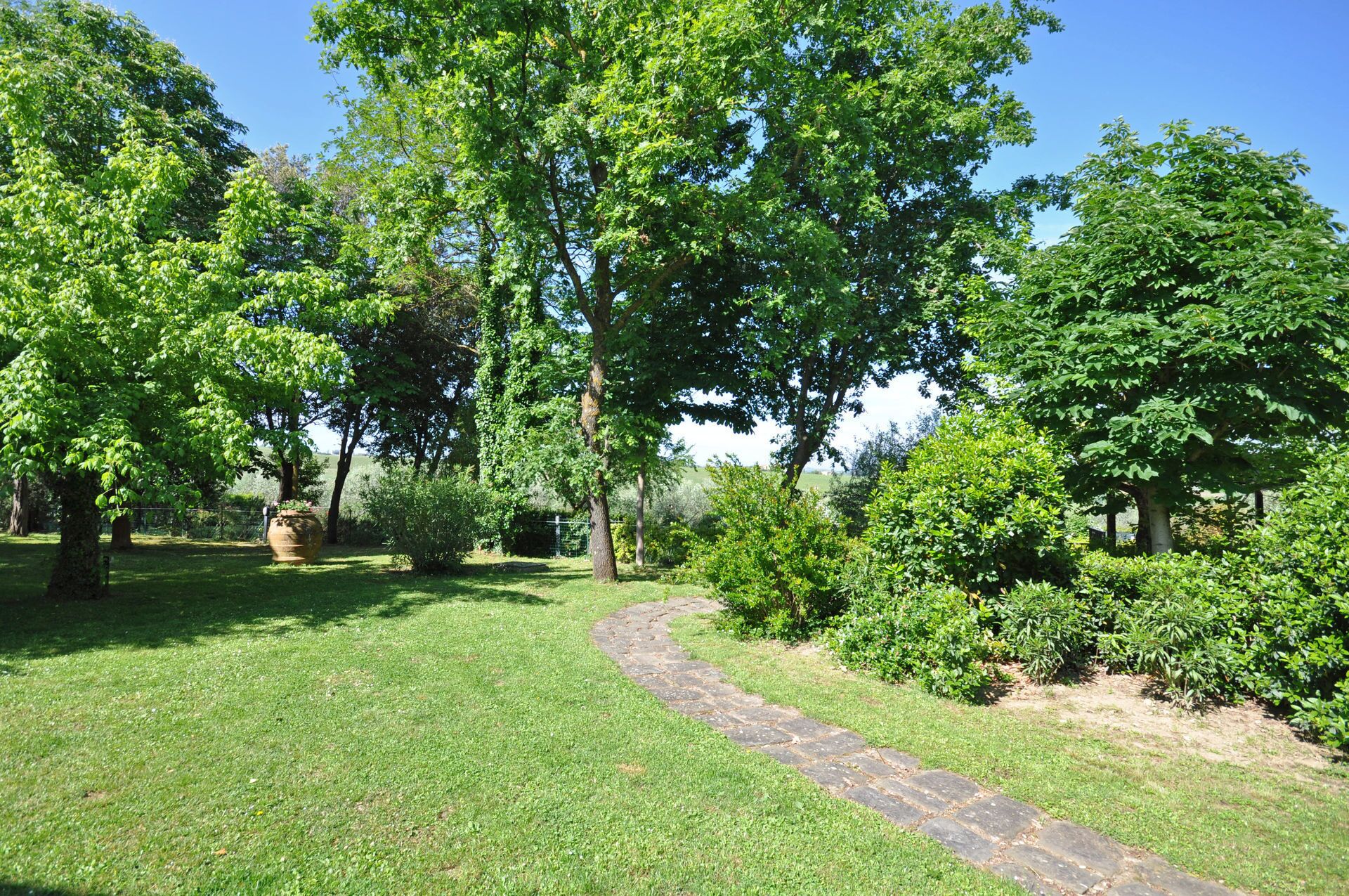 A stone pathway winding through a well-maintained grassy area with various trees and shrubs.