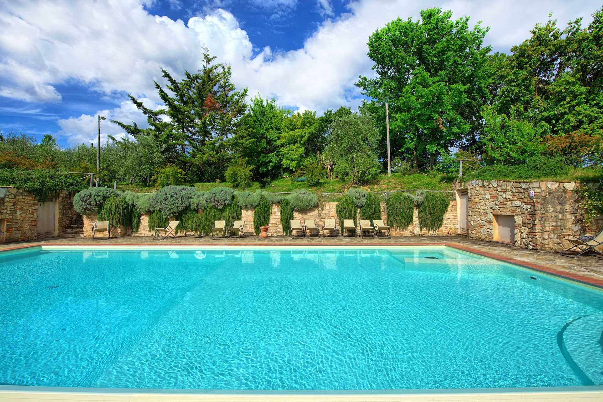 Une piscine avec des chaises longues et un mur en pierre agrémenté de verdure.