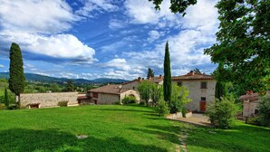 Un bâtiment en pierre, typique des zones rurales, avec un toit en tuiles, entouré d’une végétation luxuriante et d’arbres.