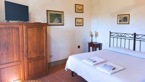 Une chambre à coucher avec une armoire en bois, un lit avec du linge de lit blanc, une petite table de chevet avec une lampe, et trois tableaux encadrés accrochés au mur.