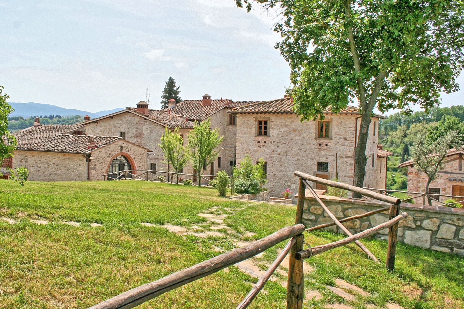 A stone building with a tiled roof, surrounded by a grassy area and trees.