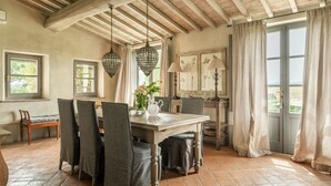 A dining area with a wooden table, grey upholstered chairs, hanging crystal chandeliers, and a view of the outdoors through large windows. - Villa Danilo - Luxury Holiday Villa with private swimming pool in San Casciano dei Bagni, Orcia ... (San Casciano Dei Bagni)