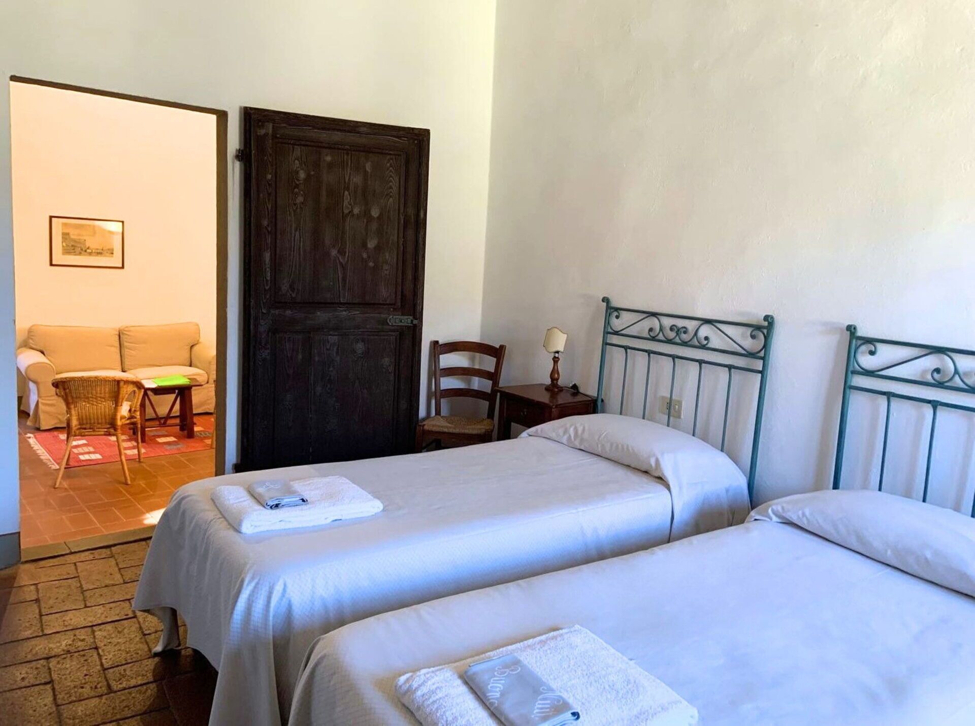 Ein Zimmer mit zwei Betten, einer Holztür, einem Sessel, einem kleinen Tisch mit Lampe und einem Sofa.