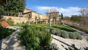 A stone building with a stone staircase leading to a door, surrounded by a well-maintained garden with various shrubs and a clear sky. - Dante 5 - Apartment with swimming pool (Volterra)