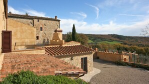 A stone building with a tiled roof, a small garden area, and a view of rolling hills in the background. - Dante 5 - Apartment with swimming pool (Volterra)