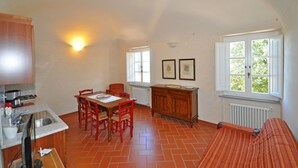 A kitchen with a dining table, chairs, a stove, and a radiator. There are two windows with curtains and a wall-mounted light. - Dante 5 - Apartment with swimming pool (Volterra)