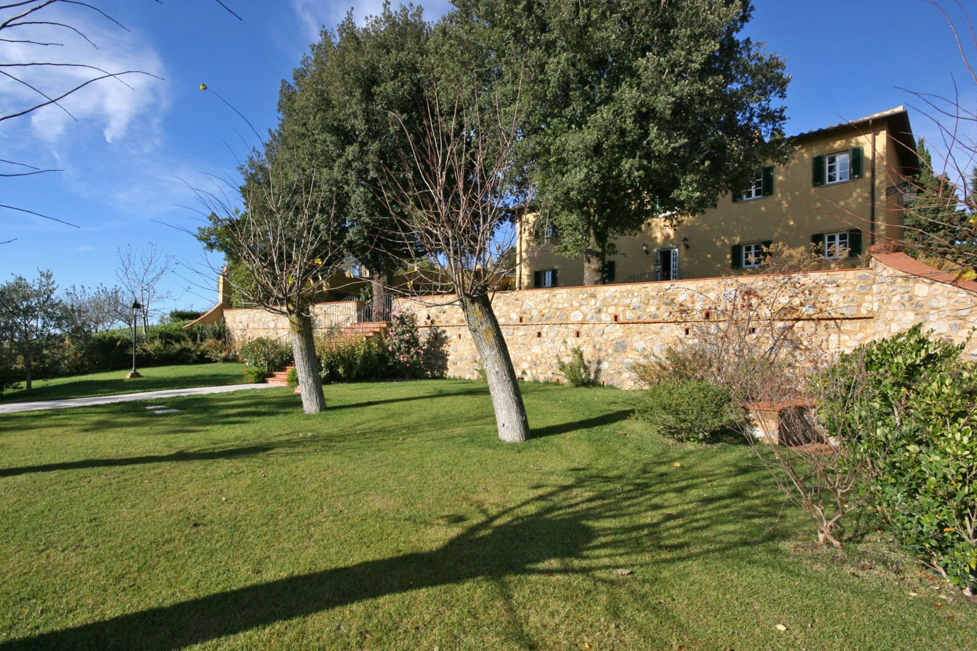 A stone building with a stone wall, a grassy lawn, and trees.