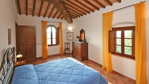 Un dormitorio con cama, vigas de madera en el techo, un aparador, una ventana con cortinas y una puerta.