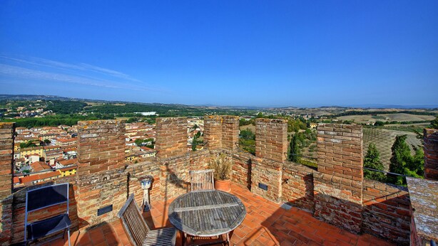 Terraza en la azotea con una mesa y sillas, con vistas a una pared de ladrillo histórica y a un pueblo más abajo.