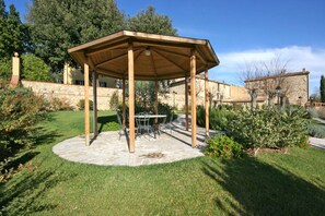 Un belvédère en bois doté d’un sol en pierre, entouré d’un jardin bien entretenu et de murs en pierre.