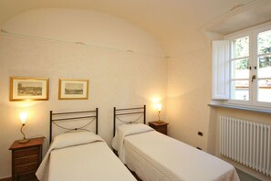 Une chambre avec deux lits simples, une table de chevet avec une lampe, une fenêtre donnant sur un paysage agréable et deux tableaux encadrés accrochés au mur.