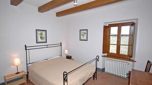 Un dormitorio con cama, mesita de noche, lámpara, ventana con vistas y radiador.
